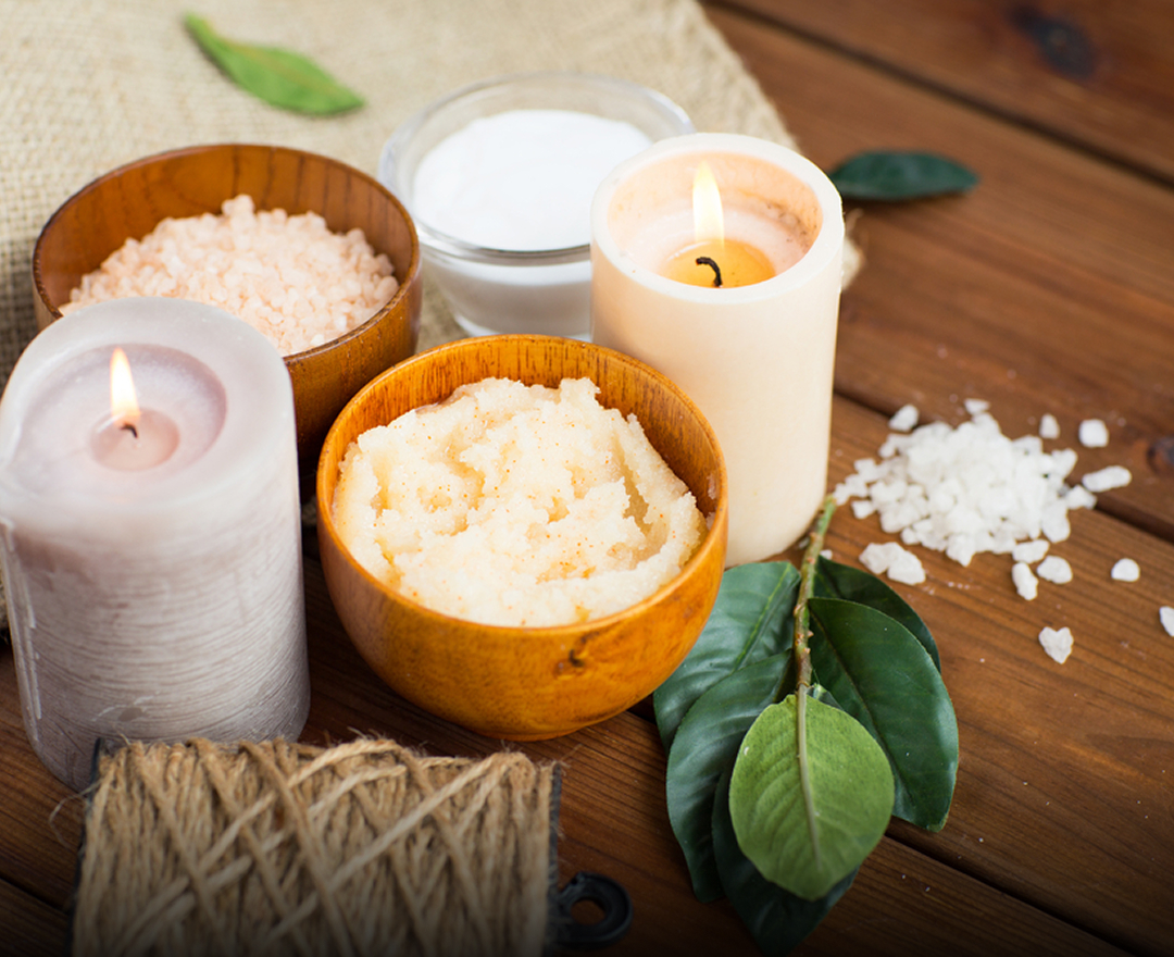 A wooden table displays an assortment of bath salts and candles in various shapes and colors, creating a relaxing ambiance.