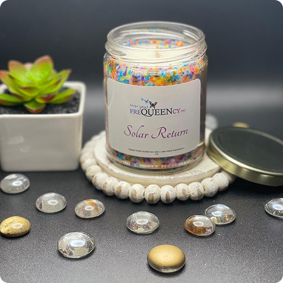 A jar of colorful sprinkles next to a small green plant on a wooden table.