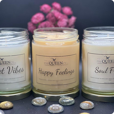 Three jars of scented candles in varying colors, each labeled with its unique fragrance, arranged on a wooden surface.